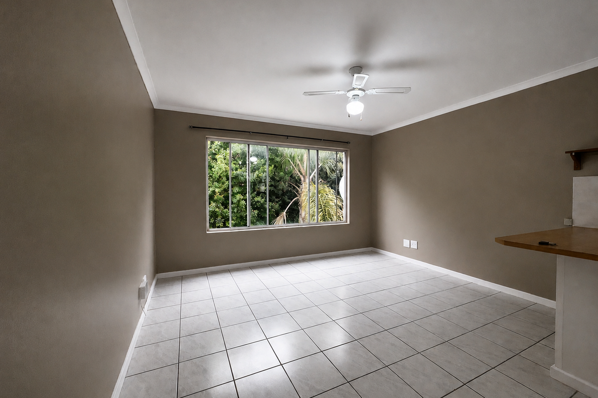 An open-plan living area featuring neutral wall tones, tiled flooring, a ceiling fan, and a breakfast bar overlooking a garden view.