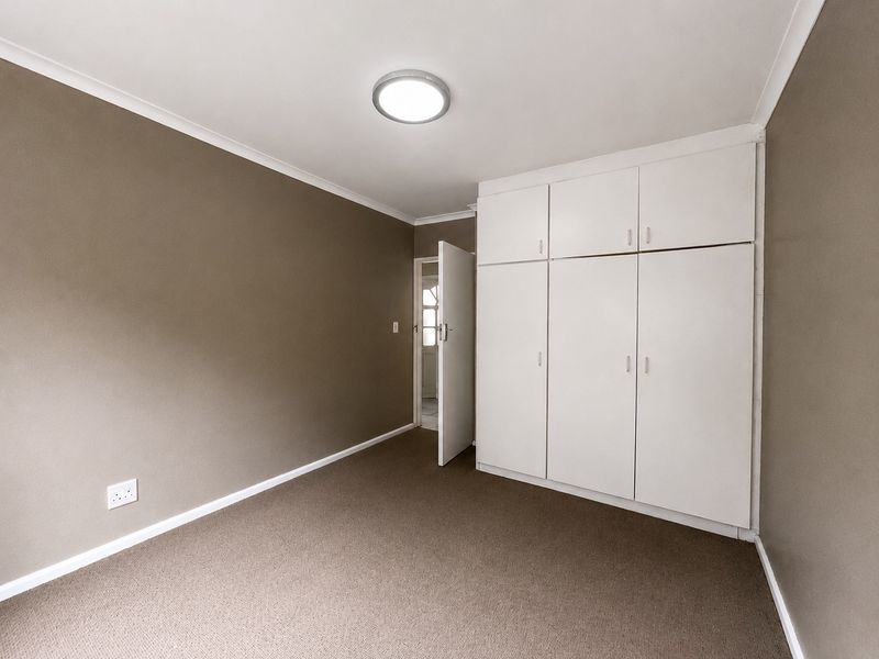 A clean, empty bedroom featuring neutral wall tones, carpeted flooring, and ample built-in cupboard storage space.