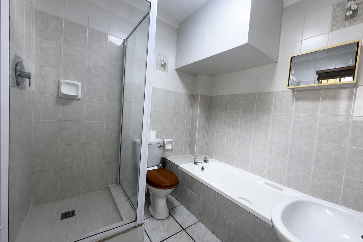 A functional bathroom featuring a separate shower enclosure, bathtub, toilet, and washbasin with neutral wall and floor tiling.