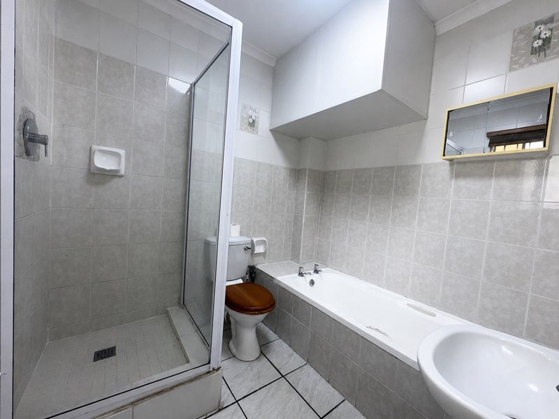 A functional bathroom featuring a separate shower enclosure, bathtub, toilet, and washbasin with neutral wall and floor tiling.