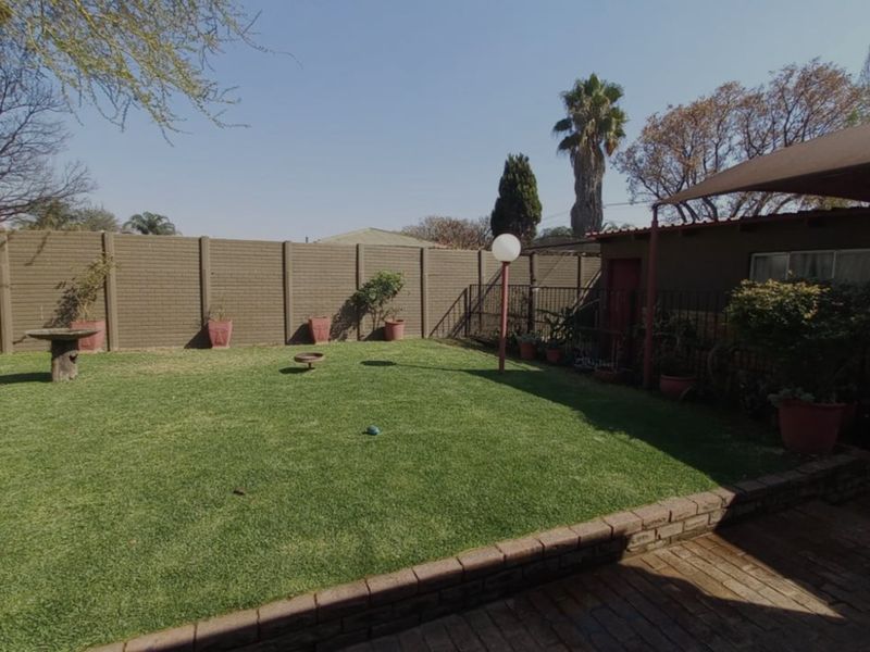 A well-maintained private garden featuring a lush lawn, a brick-paved patio area, and a secure precast concrete boundary wall.