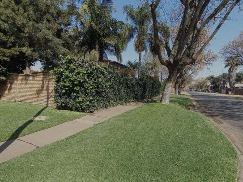 A street-level view showing the property's brick boundary wall, landscaped verge, and paved sidewalk along a residential road.