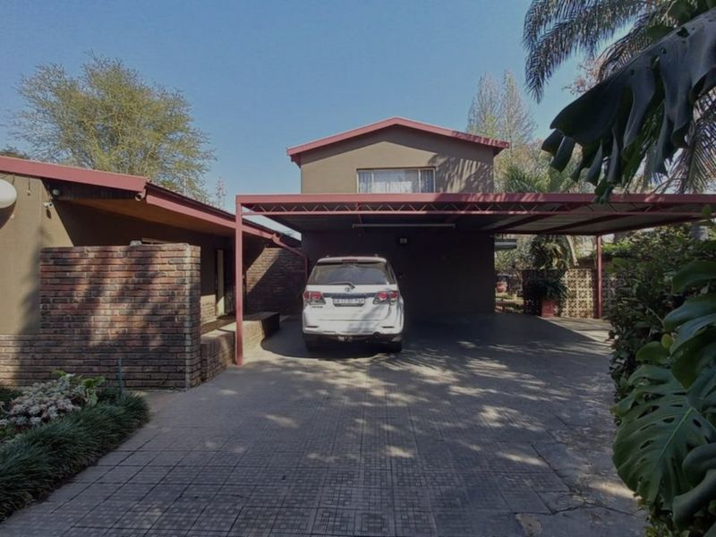 Front elevation of the property featuring a paved driveway, a covered carport, and a combination of brick and painted exterior finishes.