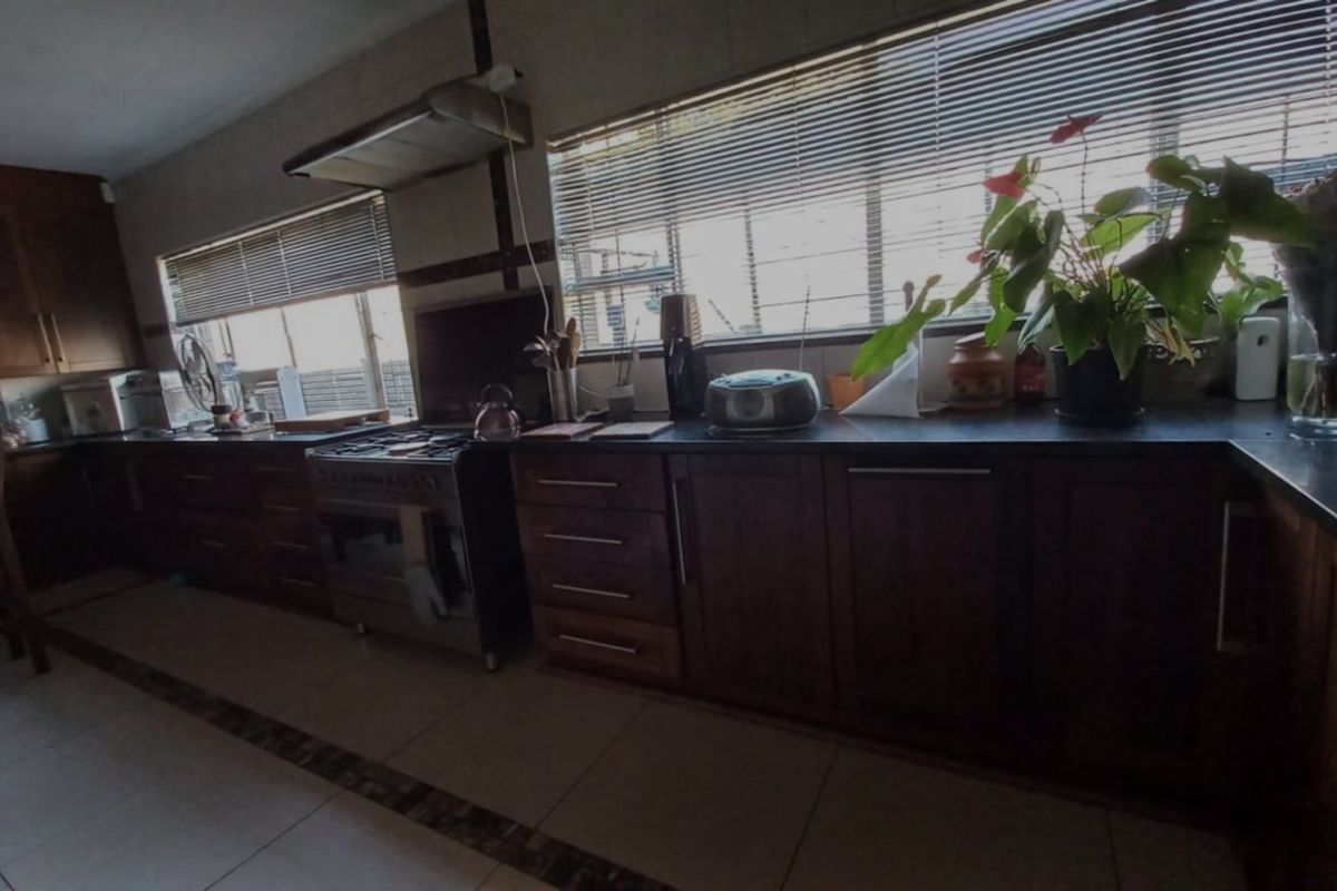 A functional kitchen featuring dark wood cabinetry, a stainless steel gas stove with extractor fan, and tiled flooring with large windows.