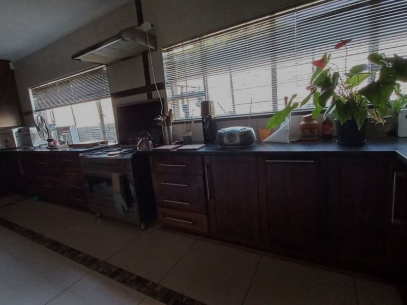 A functional kitchen featuring dark wood cabinetry, a stainless steel gas stove with extractor fan, and tiled flooring with large windows.