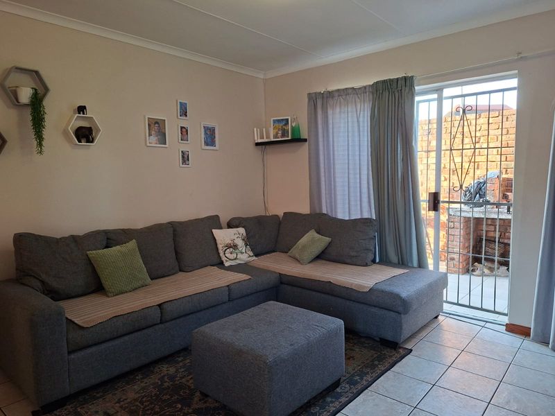 A comfortable living room featuring tiled flooring and a sliding glass door with a security gate providing access to the outdoor patio area.