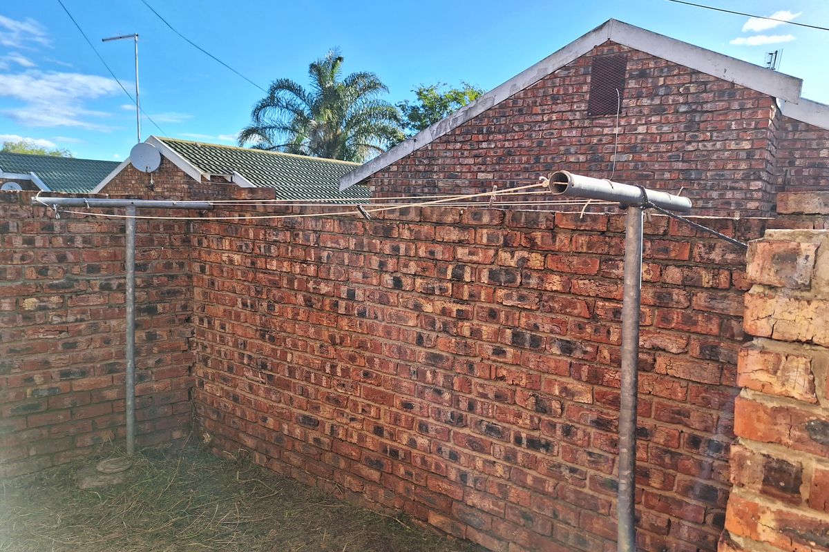 A rear exterior area featuring a face brick boundary wall and a fixed metal washing line structure.