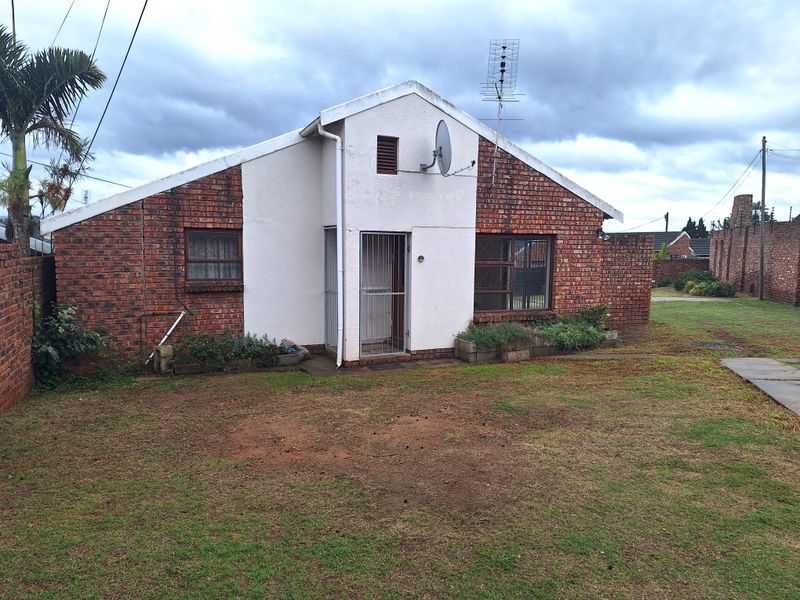 Rear view of a single-story brick house featuring a small garden, security gate, and satellite dish installation.