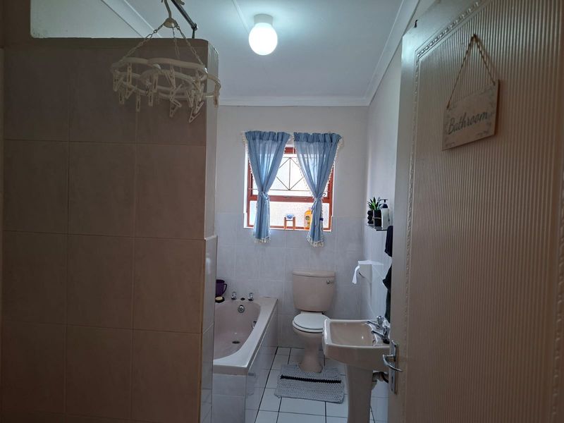 A functional bathroom featuring a bathtub, pedestal basin, and toilet with tiled flooring and wall splashbacks.