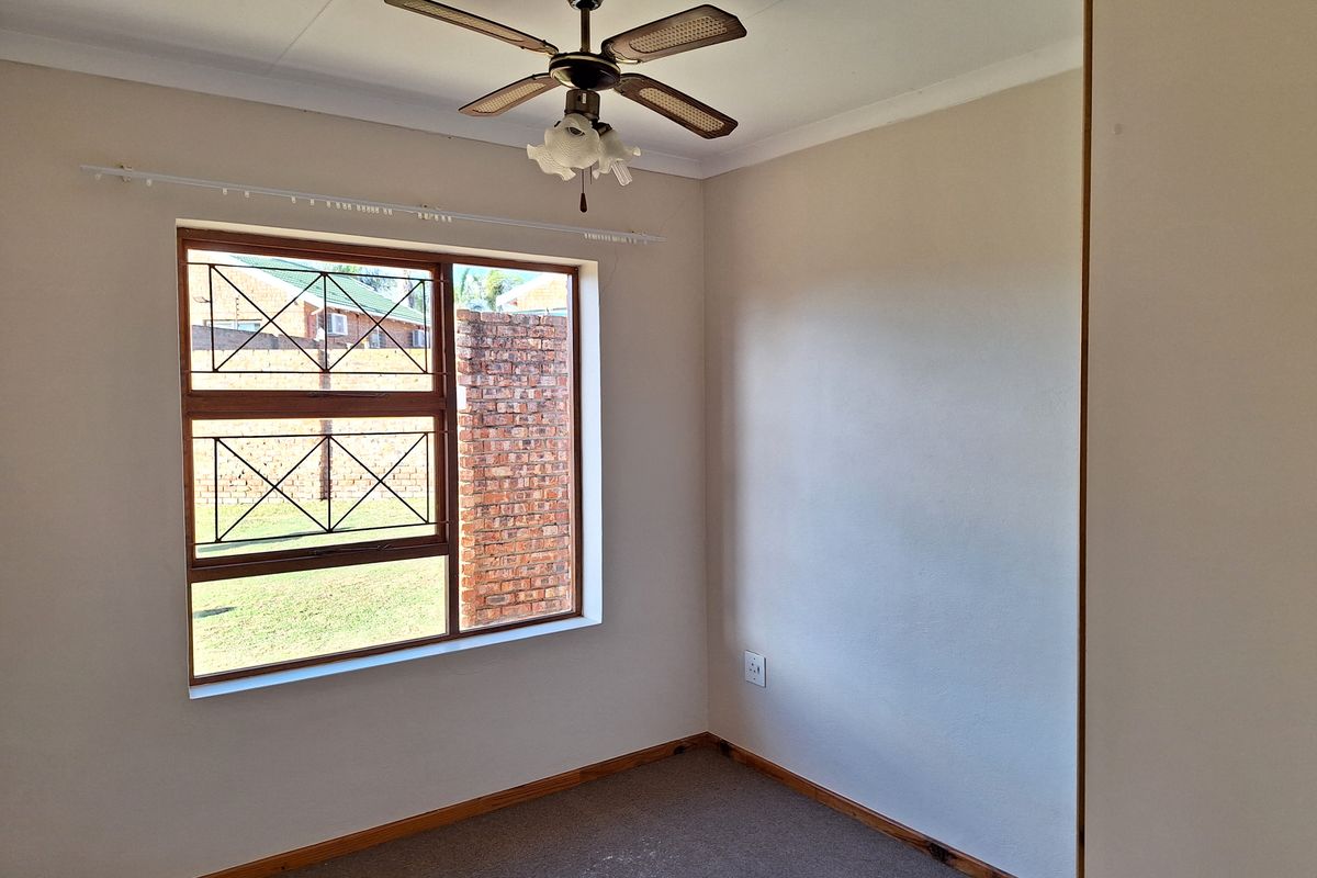 A clean, empty bedroom featuring a ceiling fan, built-in cupboard, and security bars on the window.