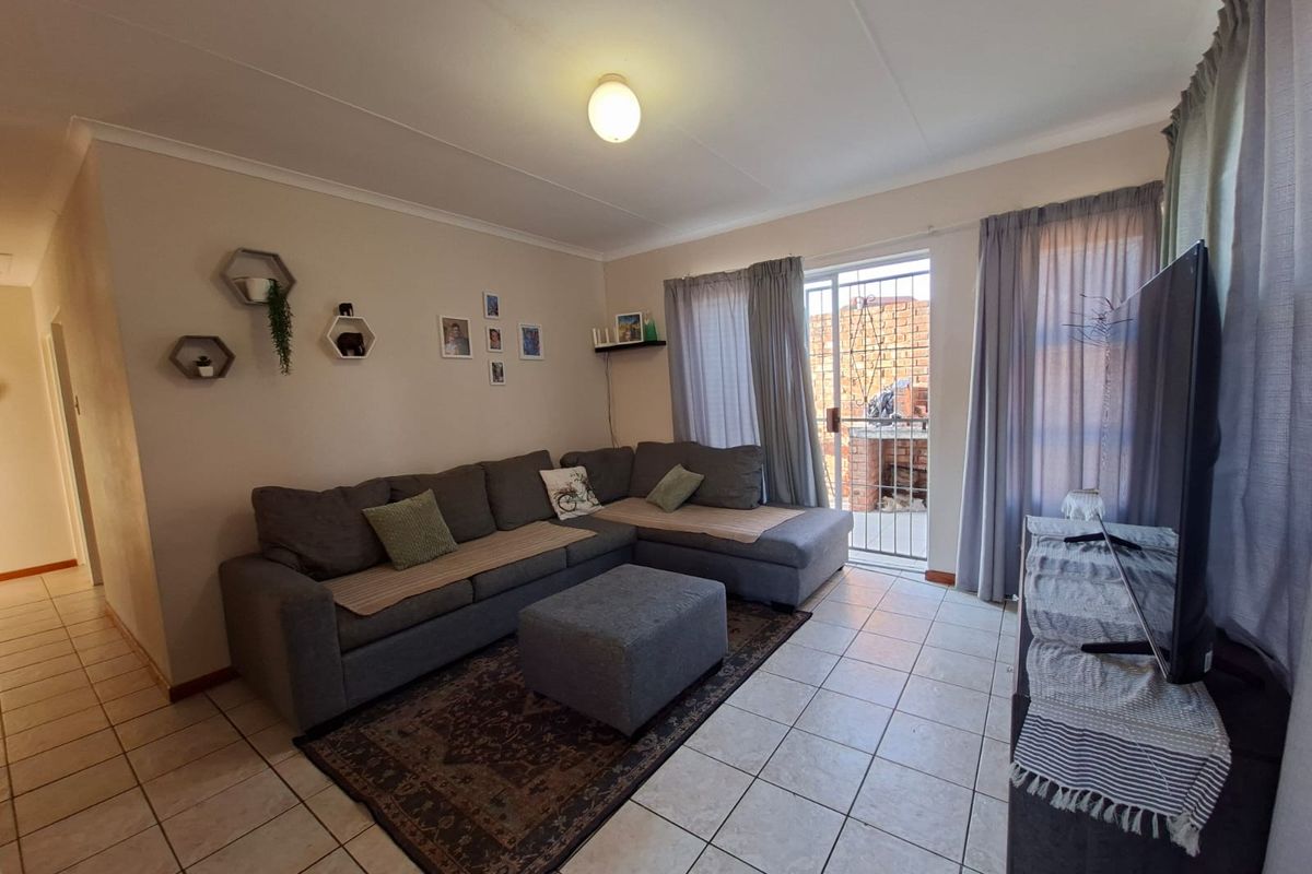 A functional living room featuring tiled flooring, neutral walls, and a sliding door providing access to an outdoor area with a security gate.