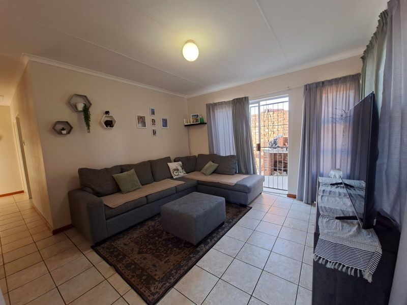 A functional living room featuring tiled flooring, neutral walls, and a sliding door providing access to an outdoor area with a security gate.