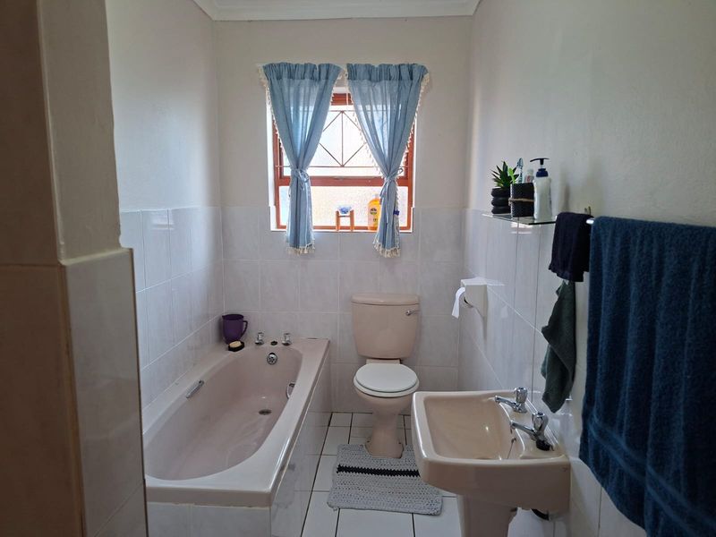 A functional bathroom featuring a bathtub, pedestal basin, and toilet with neutral wall and floor tiling.