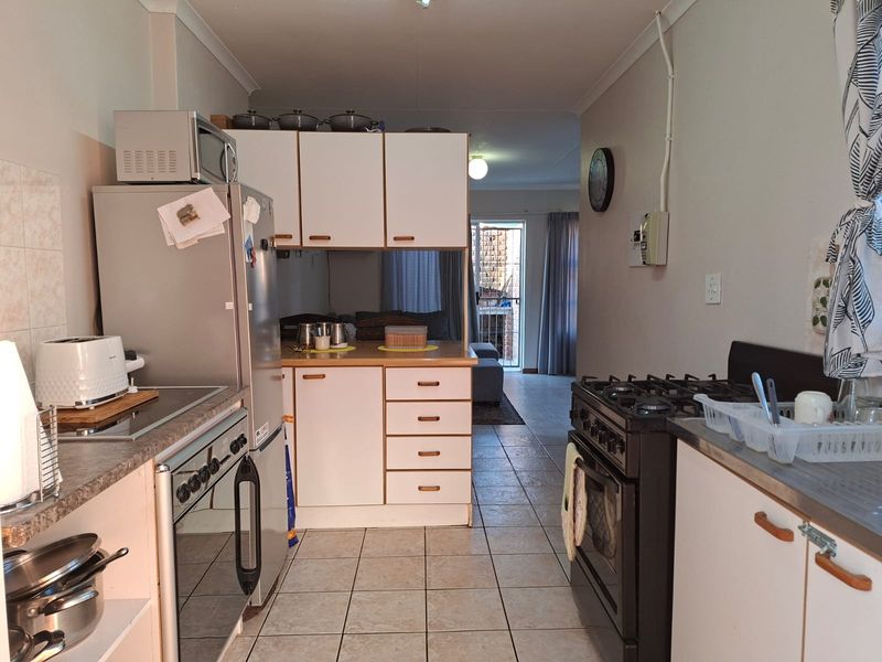 A functional kitchen featuring laminate countertops, built-in cabinetry, and a gas stove, with tiled flooring and direct access to the living area.