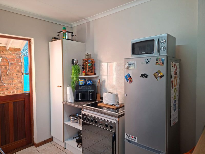 A compact kitchen area featuring a built-in oven, electric hob, tiled splashback, and a tall pantry cupboard, with direct access to an outdoor area.
