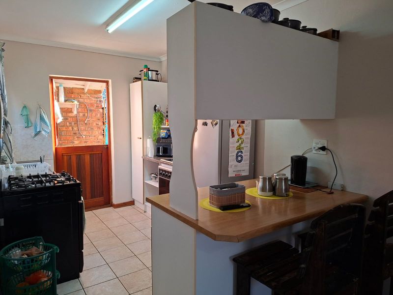 A functional kitchen featuring a breakfast bar, tiled flooring, and a gas stove, with direct access to an exterior brick-walled area.