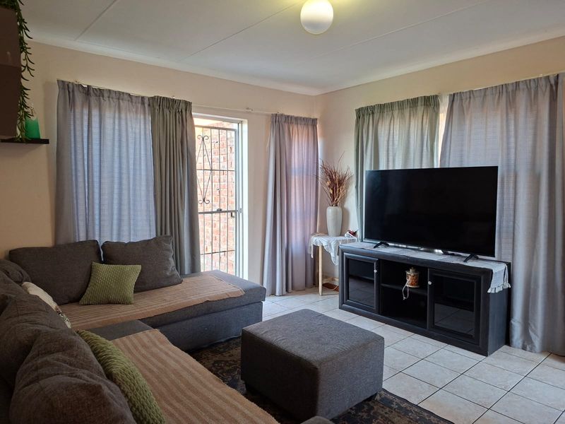 A comfortable living room featuring tiled flooring, neutral wall tones, and direct access to an exterior area through a secure door.