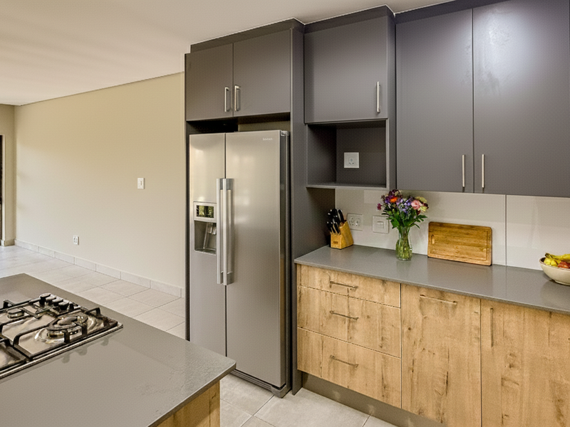 Modern open-plan kitchen featuring sleek grey and wood-tone cabinetry, stone countertops, and a gas hob, seamlessly flowing into the adjacent living area.