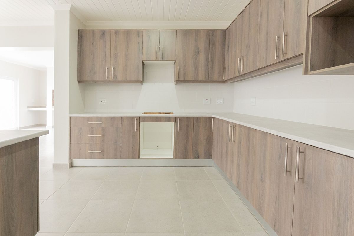 A modern, empty kitchen featuring light wood-look laminate cabinetry, stone countertops, and neutral tiled flooring, ready for appliance installation.