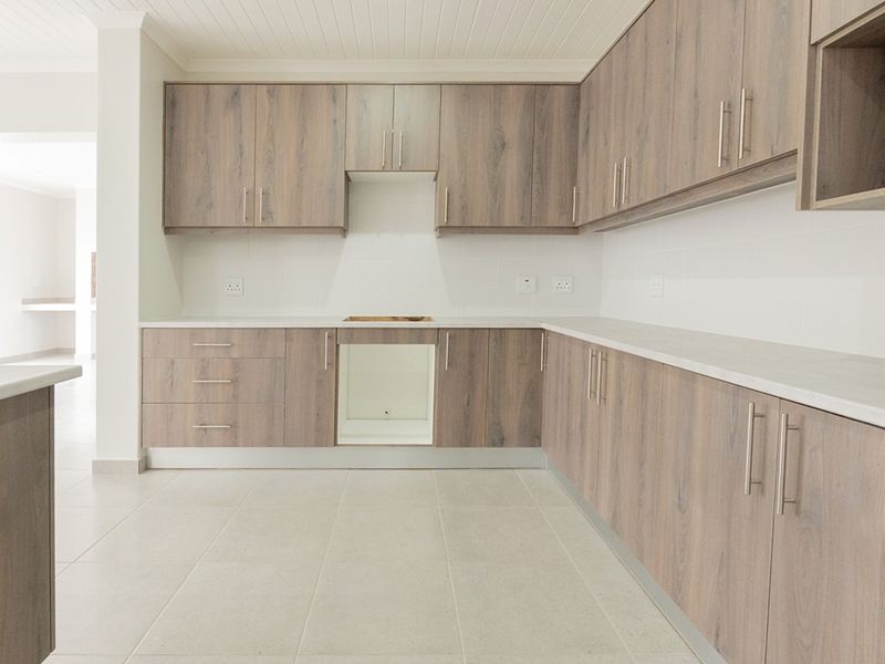 A modern, empty kitchen featuring light wood-look laminate cabinetry, stone countertops, and neutral tiled flooring, ready for appliance installation.
