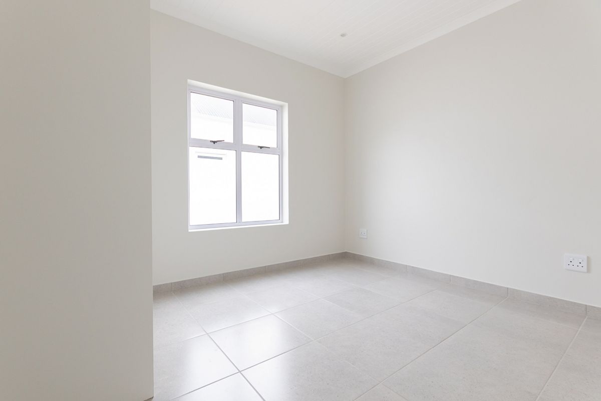 A clean, vacant bedroom featuring neutral tiled flooring, crisp white walls, and a window providing natural light.