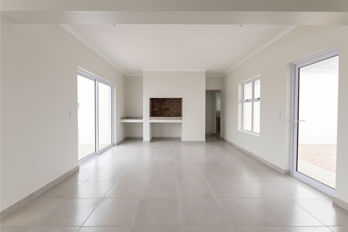 Spacious, light-filled living area featuring neutral tiled flooring, a built-in brick fireplace, and multiple sliding glass doors providing access to the exterior.