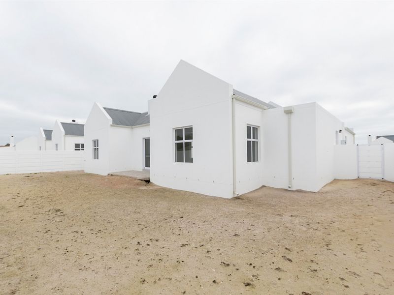 Rear view of a modern white house with a metal roof, featuring a large, unlandscaped sandy yard and perimeter boundary walls.