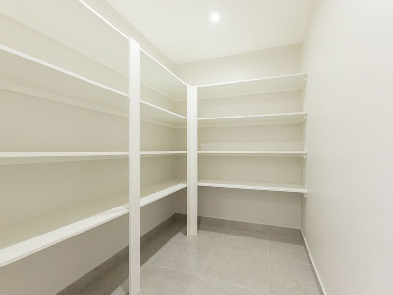 A clean, modern walk-in pantry or scullery featuring extensive built-in white shelving and neutral tiled flooring.