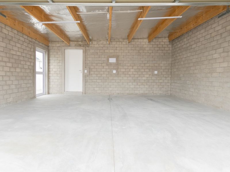 A clean, spacious, and unfinished garage featuring exposed timber rafters, concrete block walls, and a smooth concrete floor.