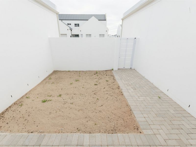 A compact rear courtyard featuring a paved walkway and an unlandscaped sandy garden area enclosed by high boundary walls.