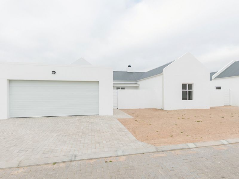 Modern single-story house exterior featuring a clean white facade, a double garage, and a paved driveway with an unfinished garden area.