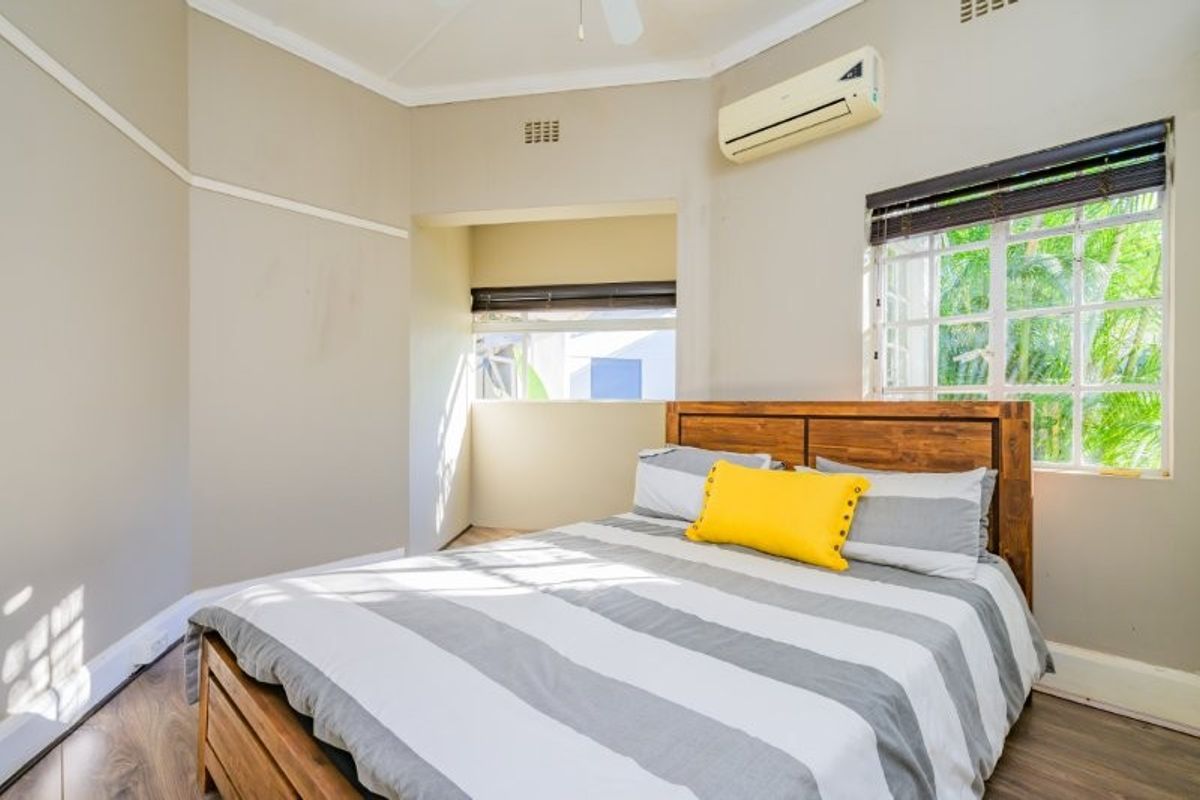 A well-lit bedroom featuring laminate flooring, a split-system air conditioner, and a ceiling fan, offering a comfortable and functional living space.