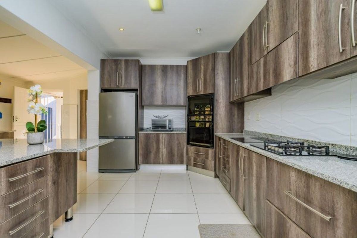 Modern kitchen featuring wood-look laminate cabinetry, granite countertops, a built-in oven, gas hob, and clean tiled flooring.