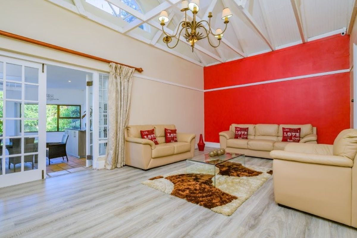 Spacious living room featuring a vaulted ceiling with exposed rafters, a skylight, and double french doors leading to an adjacent room.