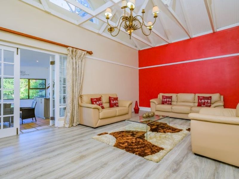 Spacious living room featuring a vaulted ceiling with exposed rafters, a skylight, and double french doors leading to an adjacent room.