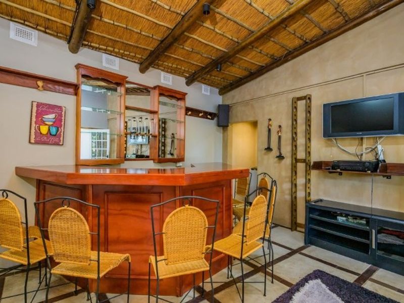 A dedicated bar area featuring a built-in wooden counter, mirrored back bar, and a rustic thatch ceiling with exposed timber beams.