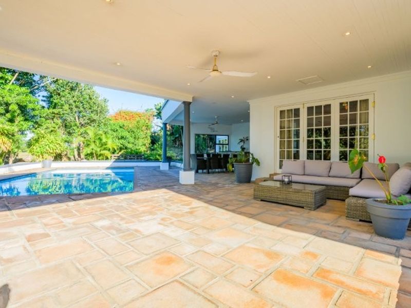 Spacious covered patio area featuring stone paving, recessed lighting, and a ceiling fan, overlooking a private swimming pool.