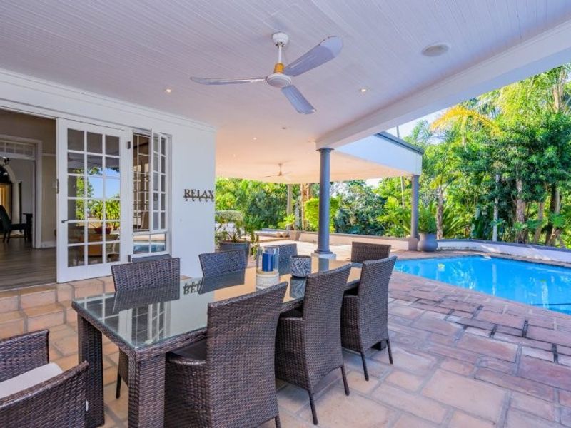 Spacious covered patio featuring stone flooring, ceiling fans, and recessed lighting, overlooking a private swimming pool and lush garden area.