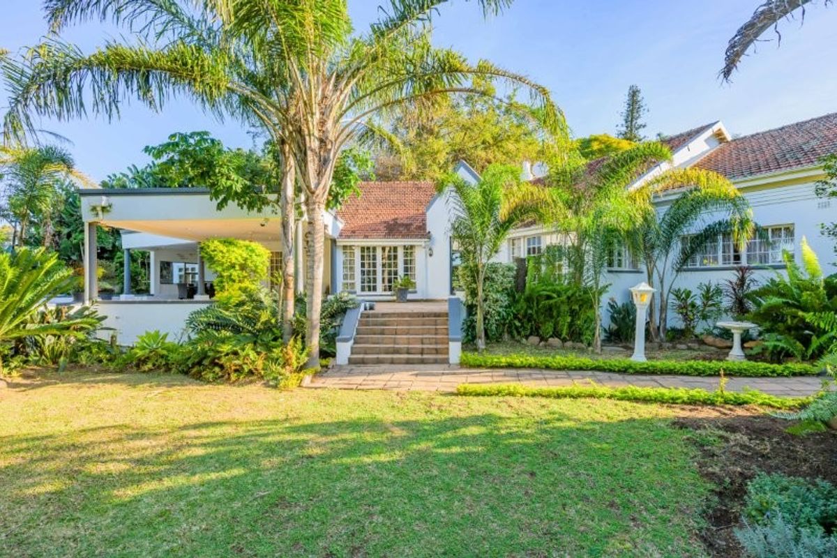 A well-maintained rear exterior view featuring a landscaped garden, paved walkway, concrete stairs leading to the home, and a covered patio area.