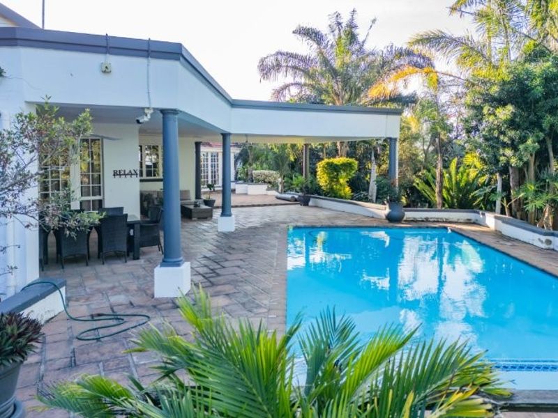 Spacious outdoor entertainment area featuring a swimming pool and a large covered patio with stone paving, ideal for relaxation and outdoor dining.