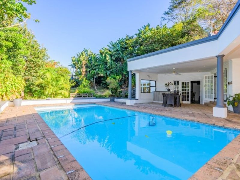 A well-maintained outdoor pool area featuring a paved deck and a spacious covered patio, perfect for outdoor entertaining and relaxation.