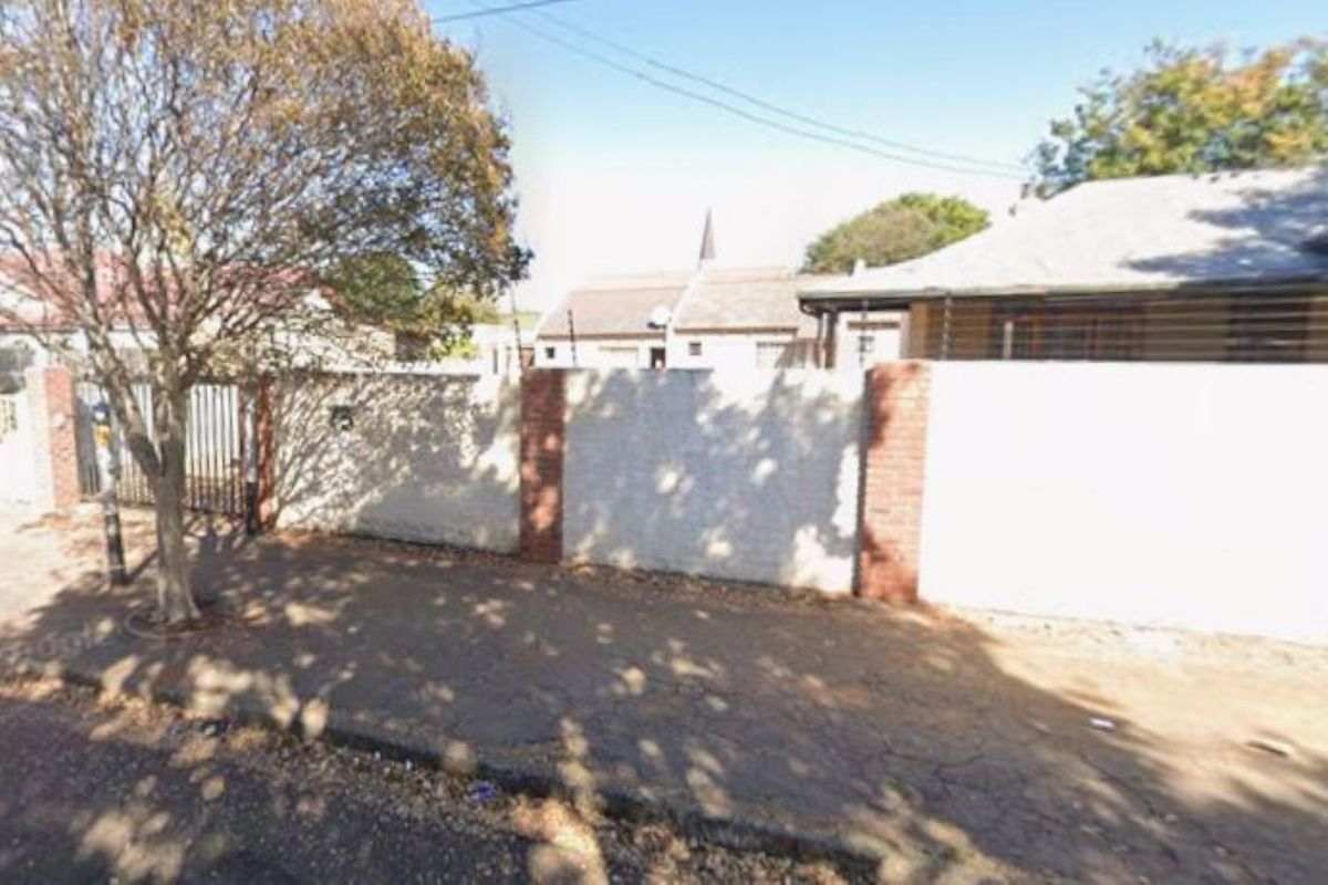 Street view of the property showing the perimeter wall, brick pillars, and metal gate entrance with electric fencing.
