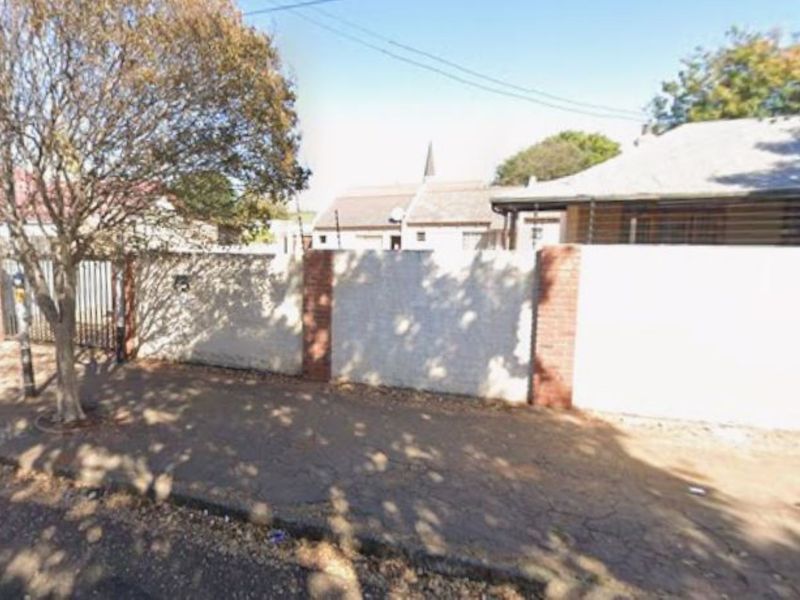 Street view of the property showing the perimeter wall, brick pillars, and metal gate entrance with electric fencing.