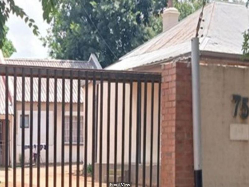 Front view of a residential property featuring a brick boundary wall, metal security gate, and a corrugated metal roof.