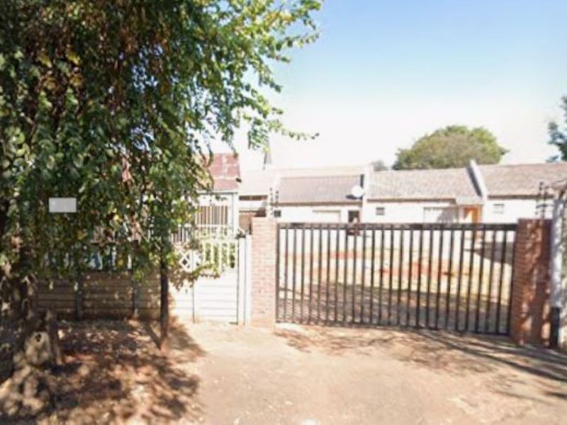 Front view of the property featuring a metal security gate, brick boundary wall with electric fencing, and a paved driveway.