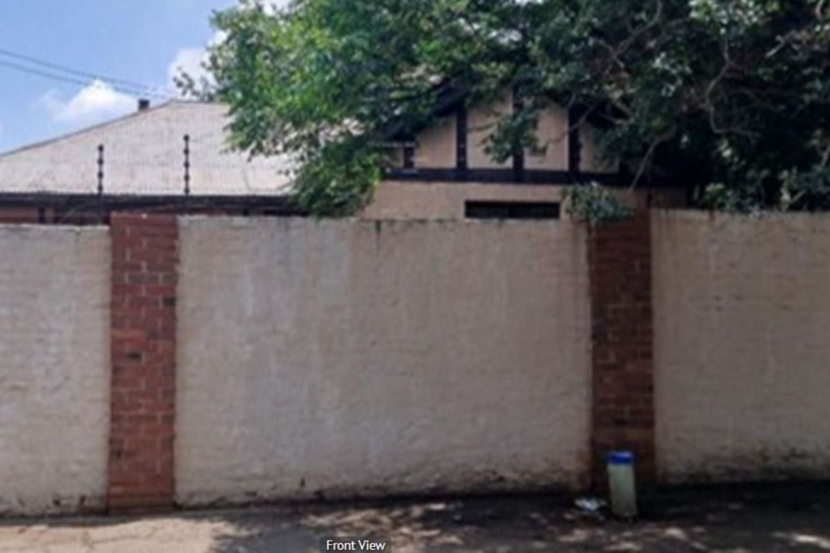 Front view of the property featuring a brick boundary wall with electric fencing and a partial view of the main house roofline.