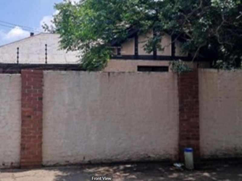 Front view of the property featuring a brick boundary wall with electric fencing and a partial view of the main house roofline.