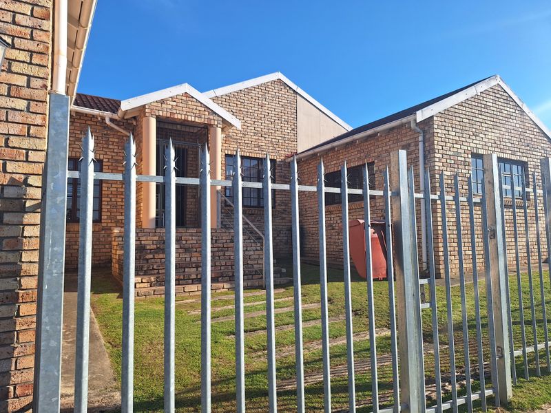 Front elevation of a face brick house featuring a covered entrance porch, concrete steps, and secure metal spike perimeter fencing.