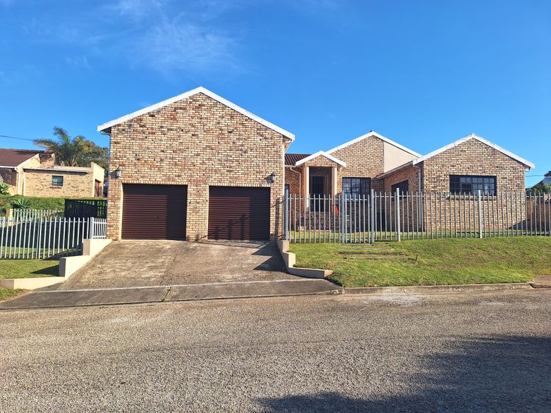Front elevation of a face-brick house featuring a double garage, concrete driveway, and secure perimeter fencing.
