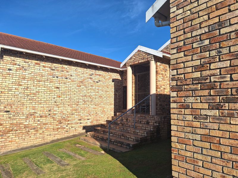 Front entrance of a face brick house featuring a covered porch with concrete steps, metal security gate, and established lawn area.